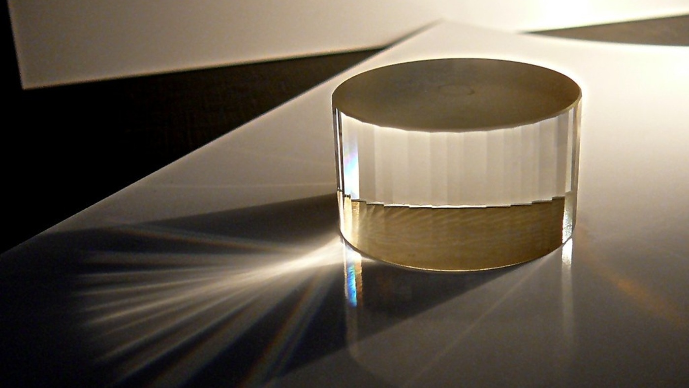 An optical-glass polygon photographed under light. An optical analogy for compact attention flexibility, not model hardware.